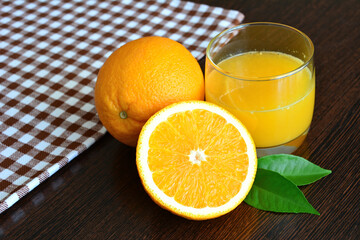 orange juice in glass with oranges on dark wooden background with plaid towel, macro