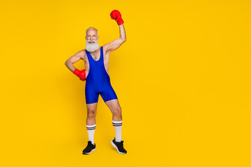 Fototapeta na wymiar Full length photo of cool lucky senior guy wear blue overall costume rising fist boxing glove empty space isolated yellow color background