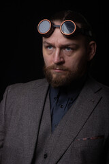 charismatic man in a classic suit and steampunk goggles on a black background stylish Portrait