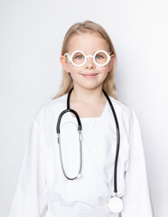 Portrait of little girl dressed up in doctor attire with stethoscope and toy glasses looking at camera