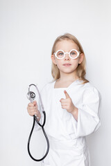 Portrait of little girl dressed up in doctor attire with toy glasses holding stethoscope, pointing with index finger up