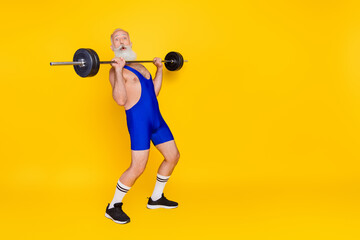 Full length portrait of sportive charismatic aged man press lifting barbell empty space isolated on yellow color background