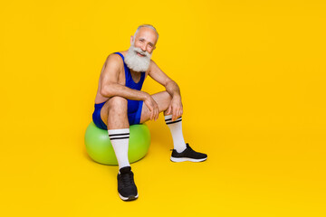 Full body photo of positive sportive person sitting fit ball enjoy dynamic workout isolated on yellow color background