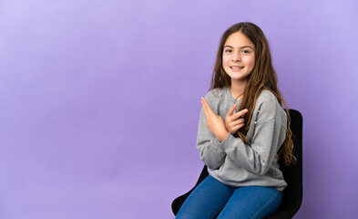 Little caucasian girl sitting on a chair isolated on purple background smiling and showing victory...
