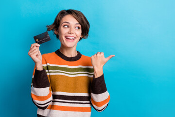 Photo of funny dreamy lady wear striped sweater holding bank card pointing thumb empty space...