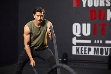 athletic young man doing exercises with battle rope in the gym