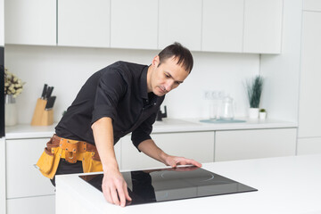 Man electrical repairs kitchen surface apartment. Installing hob in countertop. Man bought new kitchen furniture and appliances. Process installing an electrician household appliances.