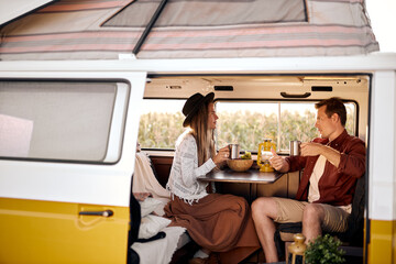 Lovely man and woman sit inside of van talking, drinking tea, discussing something during travel,...