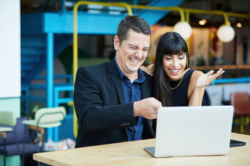 businesswoman and businessman or couple working together with laptop computer and surprised at something in a cafe