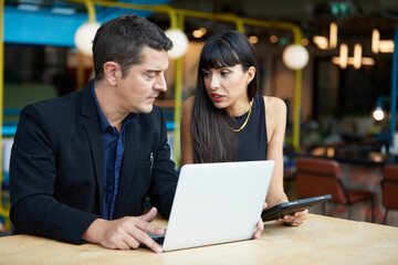businesswoman and businessman or couple talking and working together with laptop computer in a cafe