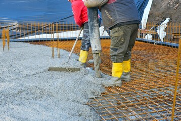 Bauarbeiter gießen die Bodenplatte eines Einfamilienhaus-Neubaus über der Baustahlmatte mit der...