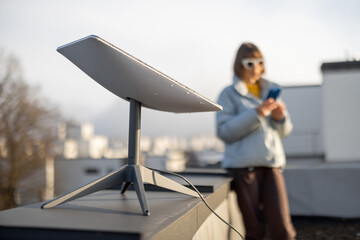LVIV, UKRAINE - January, 2023: Woman with phone uses Starlink satellite Internet, constellation operated by SpaceX on the roof of her house with satellite dish in front - 561045094