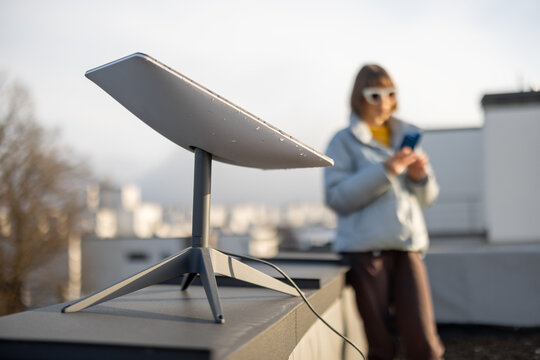 LVIV, UKRAINE - January, 2023: Woman with phone uses Starlink satellite Internet, constellation operated by SpaceX on the roof of her house with satellite dish in front
