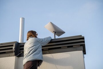LVIV, UKRAINE - January, 2023: Woman installing Starlink satellite dish on roof of her house....