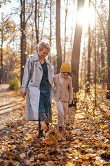 Obraz premium Happy mom and child son in warm clothes walking in autumn park in nature in fall outdoor. attractive short-haired lady enjoy spending time with son. holidays, weekends, childhood concept