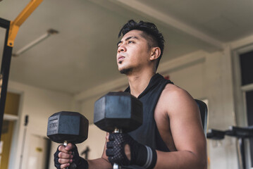 An asian man mentally preparing himself while sitting on an incline bench holding two dumbbells...