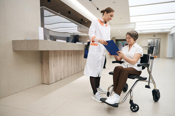 Doctor communicates with elderly woman in wheelchair at reception desk