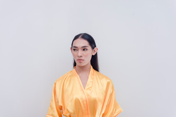 A gay cosmetics model and endorser dressed in a yellow silky bathrobe poses side view with a straight face for a studio shot isolated in a white backdrop.