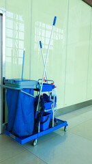 set of cleaning equipment in a blue cart parked in a corner of hallway