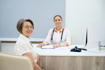 Two women in good mood are sitting in doctor office
