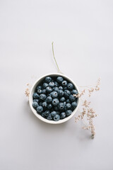 Blueberry berries in bowl on light background with dried flowers. 