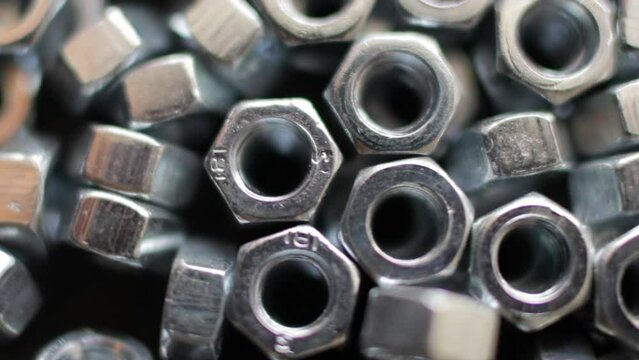Many stainless hex nuts rotating close-up. Metal industry concept.