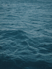 Vertical view of dark blue-green color of water surface with waves in middle of endless deep sea. Dark blue waves in deep ocean. Raging aquamarine waves on surface of the water.