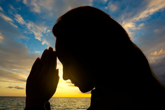 Woman's Face Backlit With Hands In Prayer