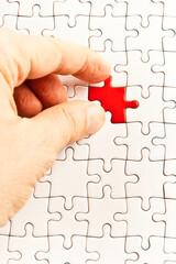 hand fitting in place a red jigsaw puzzle piece into a blank white pattern