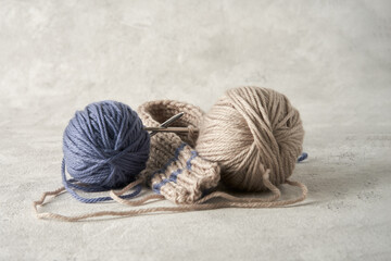Two balls of gray and blue yarn and a knitted product on knitting needles on a light gray textured...