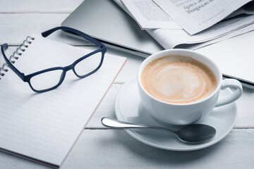 Black coffee cups, notebooks, newspapers and laptops are placed on the table. Morning news, morning preparation.