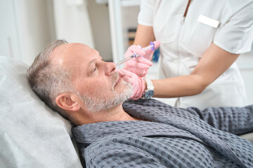 Obraz na płótnie Canvas Doctor uses modern fillers for rejuvenating course for elderly patient