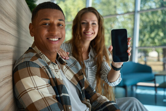 Pretty woman holding phone and sitting next to her male colleague