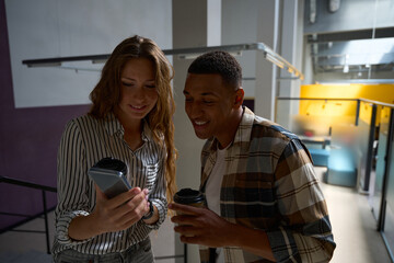 Happy colleagues holding coffee and looking at phone sreen
