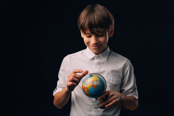 Handsome teen boy wearing white shirt holds the Earth Globe while smiling.