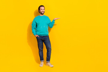Fototapeta premium Full length photo of positive good mood guy dressed teal outfit holding arm empty space isolated yellow color background
