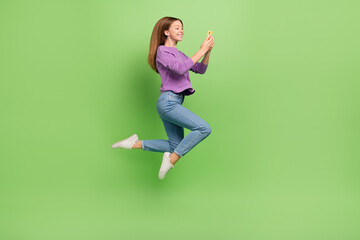 Fototapeta na wymiar Full size photo of positive cheerful girl dressed jeans purple pullover hold smartphone typing sms isolated on green color background