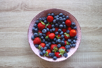 Pink rustic bowl filled with fresh blueberries and strawberries. Wooden background, top view.