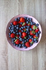 Fototapeta na wymiar Pink rustic bowl filled with fresh blueberries and strawberries. Wooden background, top view.