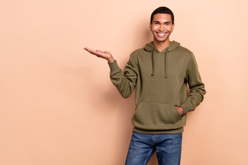 Photo of attractive charming guy dressed green khaki hoodie holding arm empty space isolated beige color background