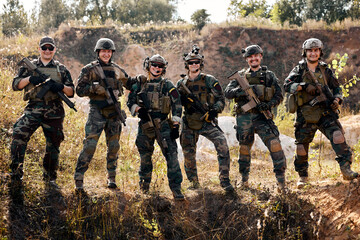 team of brave caucasian european soldiers posing at camera, looking confident, in military clothes with rifle guns, prepared for war, completely armed for attacking enemy