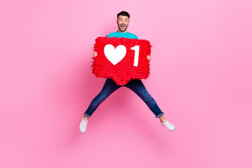 Full size photo of young nice guy jump holding heart icon pinata influencer dressed stylish blue outfit isolated on pink color background