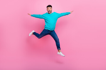 Fototapeta na wymiar Full body photo of young handsome guy jumping spread arms flying playing dressed stylish blue garment isolated on pink color background