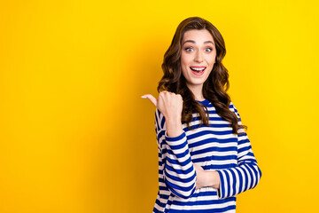 Fototapeta premium Photo of young excited overjoyed curly hair woman wear stylish striped pullover direct thumb mockup useful tips isolated on yellow color background