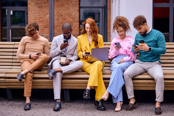 Obraz premium Group of young business workers smiling happy and confident, outdoors. Posing together with smile on face using smartphones and laptop, men and women in stylish clothes sit on bench, coworking