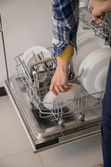Dishwasher open and a person removing the washed dishes. Concept of saving water and time in daily domestic activities.