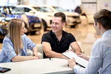 Fototapeta premium rear view on confident male manager talking to clients, explaining rules for buying car, happy married family couple sit listening to consultant, have talk discussion. in modern car dealership