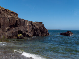 Fototapeta na wymiar A rock among the blue sea waters. Seaside landscape, rocky mountain beside body of water.
