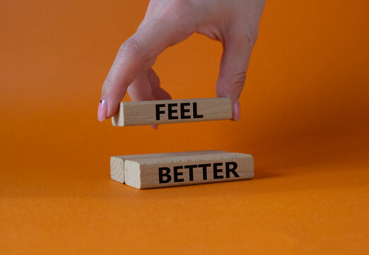 Feel better symbol. Wooden blocks with words Feel better. Businessman hand. Beautiful orange background. Business and Feel better concept. Copy space.