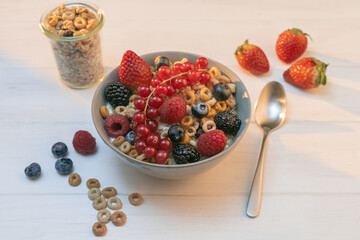 Cereal bowl with berries and spoon on a white table in the morning sunlight